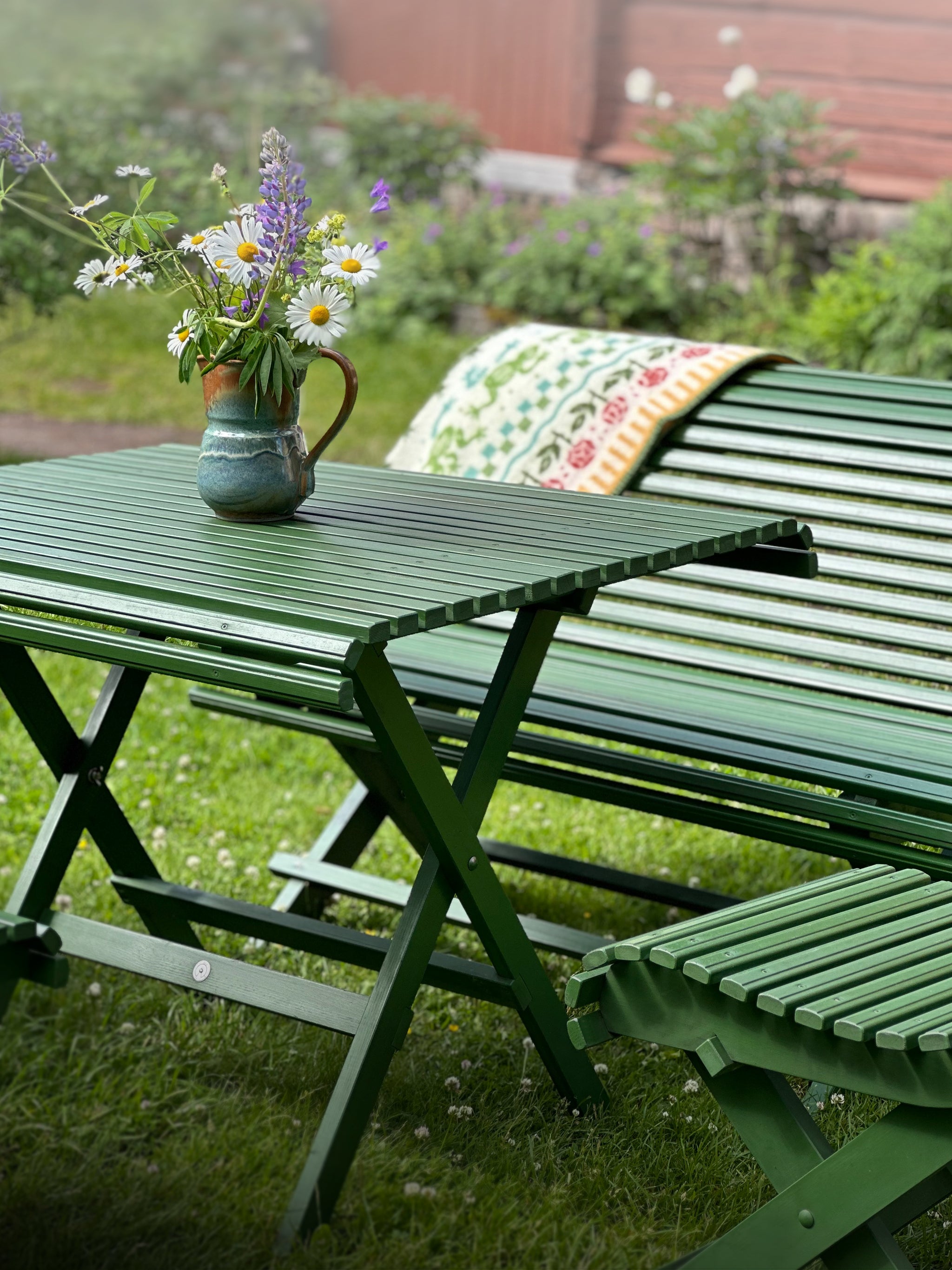 Gröna klassiska utemöbler i trä – hopfällbart trädgårdsbord och trädgårdssoffa, dekorerat med en blombukett. Carl Larsson, Sundborn