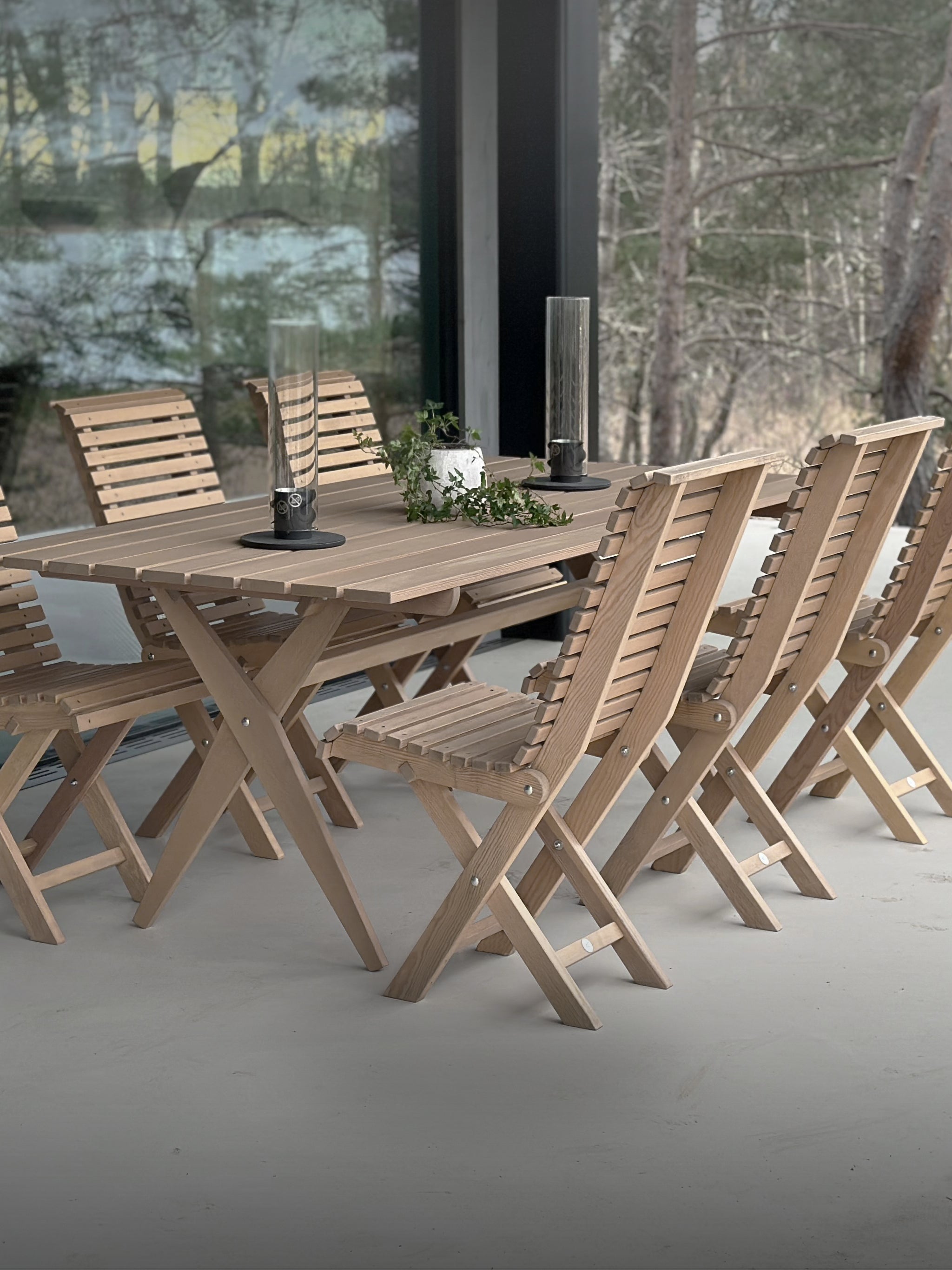Naturfärgade hopfällbara trädgårdsmöbler – stilrent matbord med stolar, placerat på en modern uteplats med panoramafönster och skandinavisk design