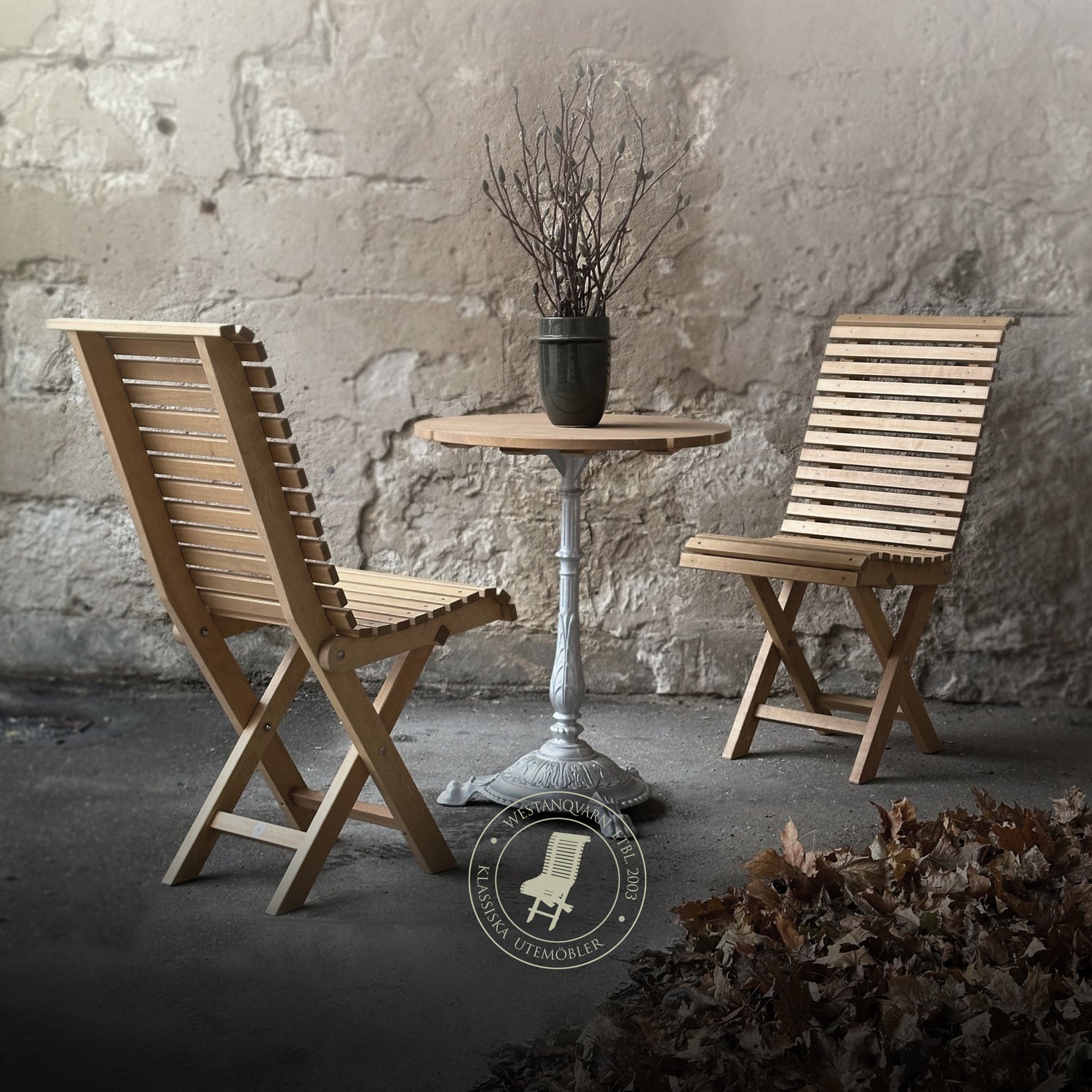 Två Villa-stolar med runt cafébord med gjuten aluminiumfot – klassiska hopfällbara utemöbler i trä, perfekta för trädgård, altan eller uteservering.